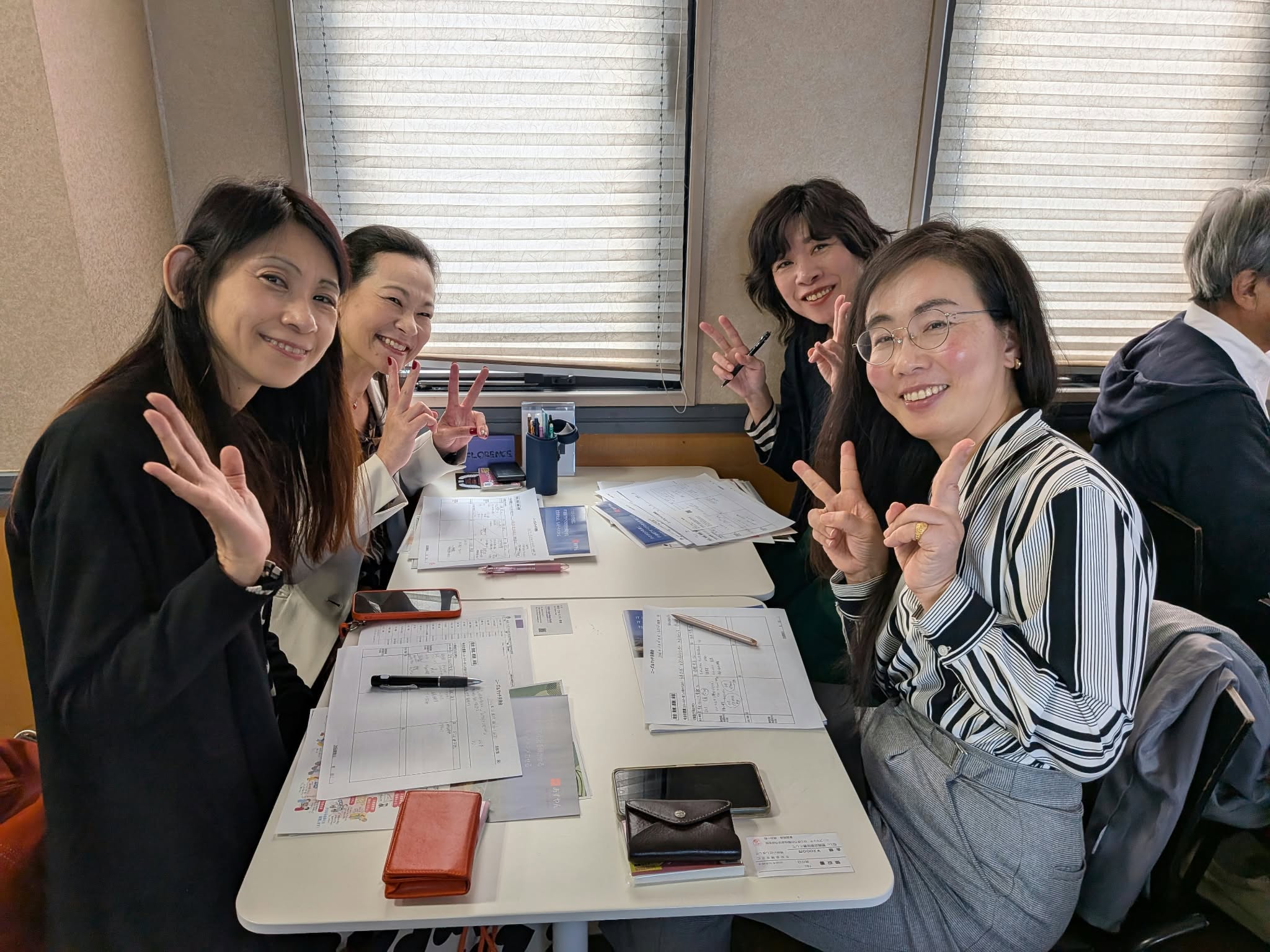 テーブルを囲み、笑顔で手を振ったりピースをしたりする参加者