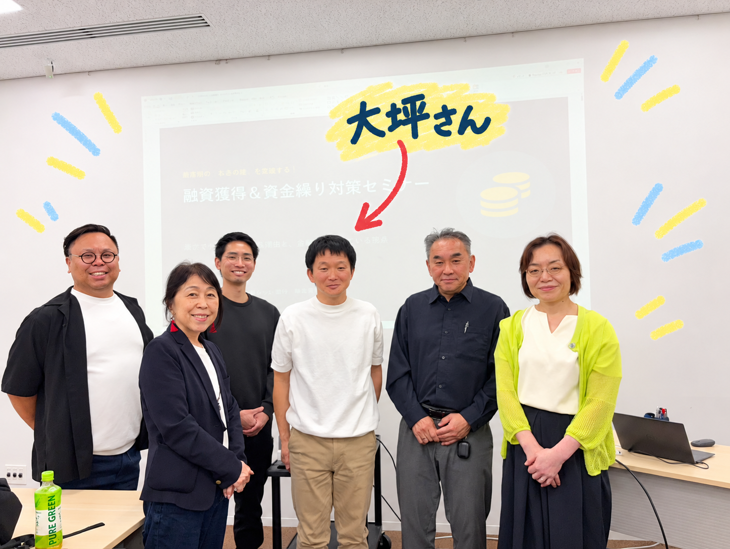 大坪和民さんと参加者の集合写真。中央の白い服の大坪さんを矢印で示しています。