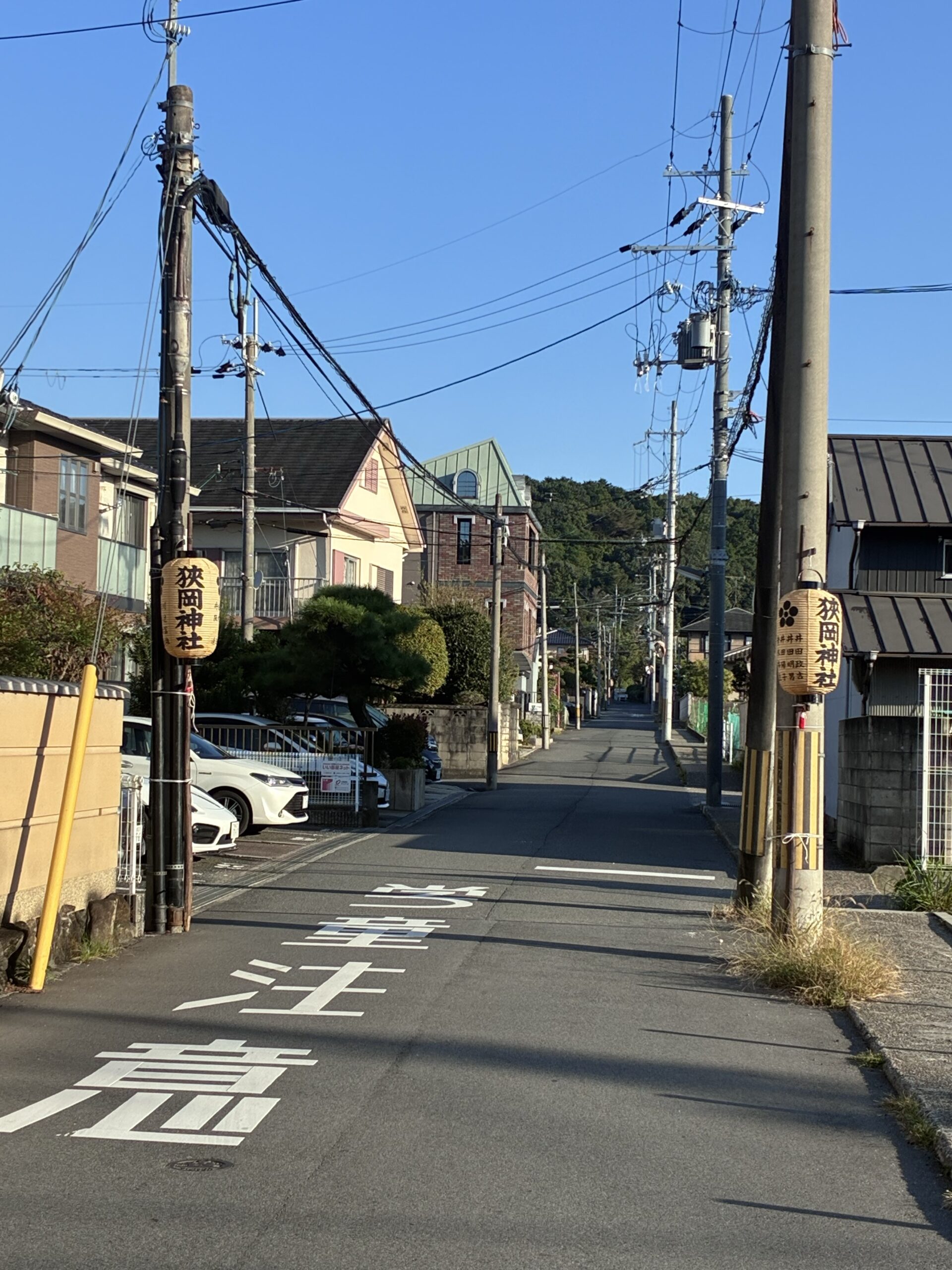 青空の下、住宅街の道の両側に掛かる狭岡神社の提灯