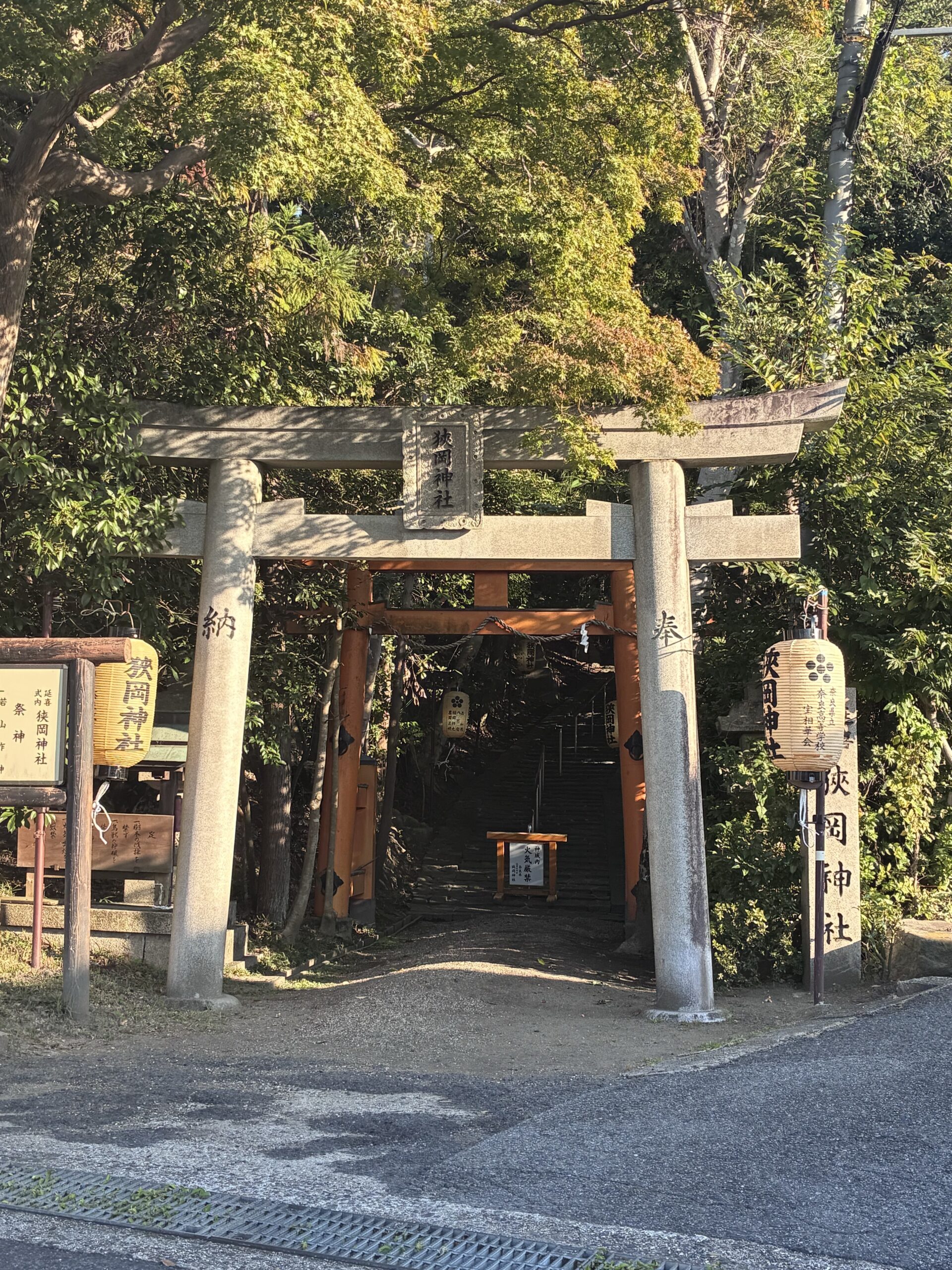 木々に囲まれた狭岡神社の入口。石の鳥居の奥に朱色の鳥居と石段が見える